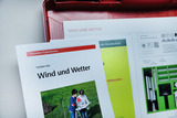 The picture shows a student kit entitled &quot;Wind and Weather&quot; that comes from a red suitcase. It contains materials and instructions for experiments to promote understanding of weather phenomena.