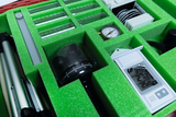 The picture shows a case with various experimental equipment inserted in green foam. The visibly included instruments include measuring cups, a thermometer and a compass, which are used for educational purposes in experiments.