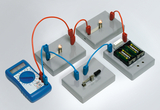 The picture shows an electrical circuit with several components, including light bulbs, batteries and a multimeter. The cables are color-coded and connect the individual components to carry out experiments in the field of electrical engineering.