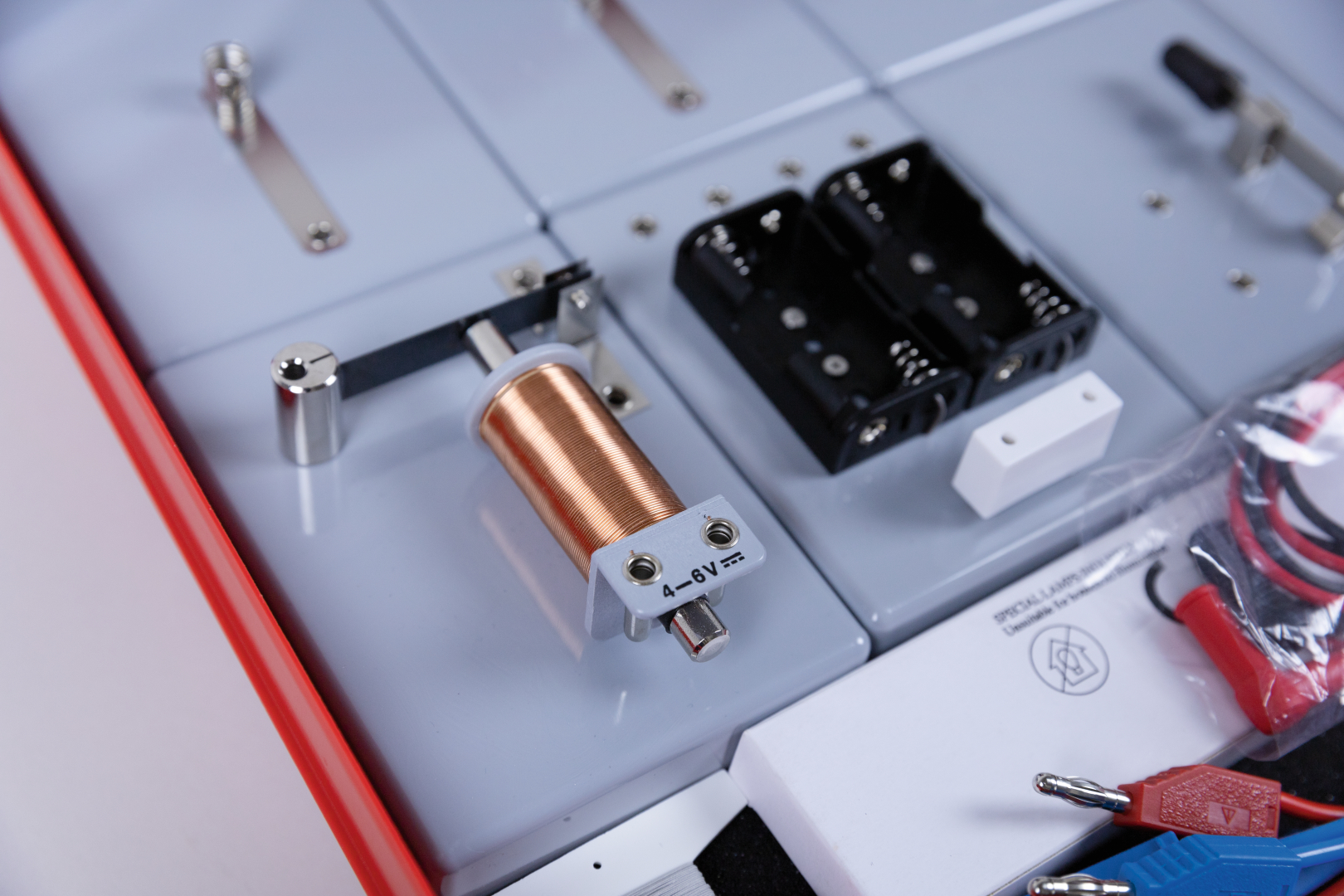 The picture shows an experiment set with a copper coil, battery compartments and various connecting cables. The equipment is suitable for practical experiments in schools to teach basic physics principles.