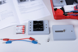 The picture shows various components of an experiment kit, including a battery holder, wire connectors and a light bulb. Also shown in a red case are a manual and other parts that can be used for educational purposes in science.