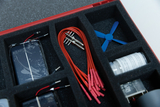 The picture shows a selection of experimental materials arranged in a red suitcase. The items included include solar panels, red connecting cables, a small propeller and other components for scientific experiments.
