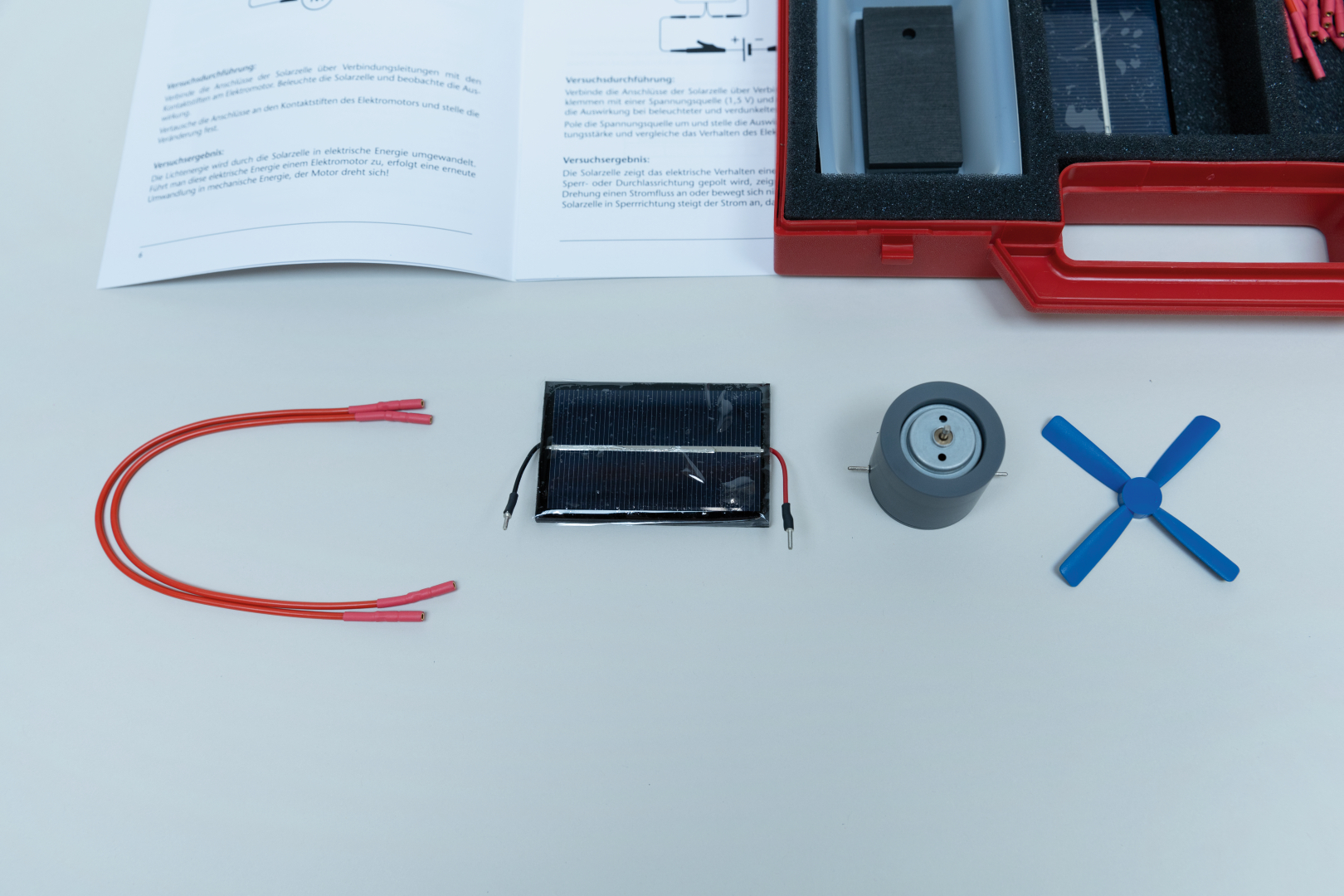 The picture shows materials for an experiment to convert solar energy into electrical energy. You can see a solar cell, a motor, connecting cables and a propeller, along with instructions for the experiment.