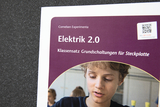 The image shows a book cover titled &quot;Electricity 2.0&quot; which presents a classroom set of basic circuits on a breadboard. It includes a QR code for support and shows a boy working on an experiment.