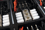 The picture shows a diverse set of experimental accessories arranged in a padded box. You can see various adapters, cables, as well as transparent and white components that are used for educational purposes in science classes.