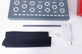 The picture shows an experiment board with several sockets and wires, which is used for physics experiments in education. Next to it are a gray pipe, a black cloth, a metal container and small parts that are part of the experiment equipment.