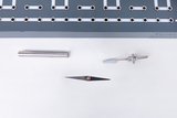 The image shows a selection of experimental materials, including a metallic rod, a thin sheet and another technical component. These objects are arranged on a white background, with a grey element with holes and lines visible in the background.