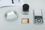 The picture shows various materials for an experiment: an aluminum bowl, iron wool in a container, a packet of matches and a digital scale. These items are typical of the experimental supplies in education.
