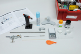 The picture shows a selection of experimental materials, including a Bunsen burner, a scale, chemicals and various tools used for chemical experiments in education. In addition, a manual and a practical box for storing the utensils are shown.