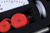 The picture shows a compact storage unit with various experimental tools for educational use. The focus is on red rollers and a measuring device that can be used for experimental applications.