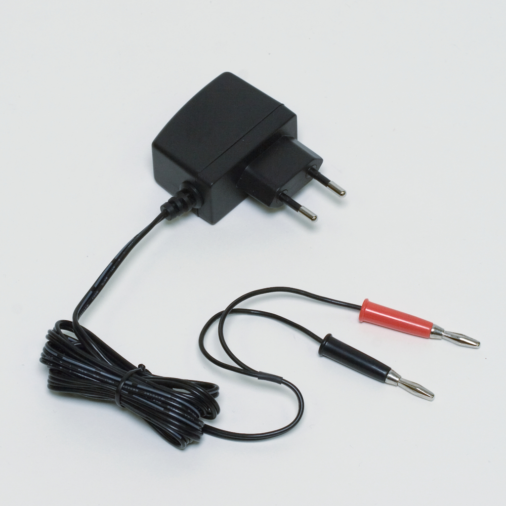 The picture shows a power supply with two cables ending in a plug. The cables are red and black and are typically intended for electrical connections or experiments in educational settings.