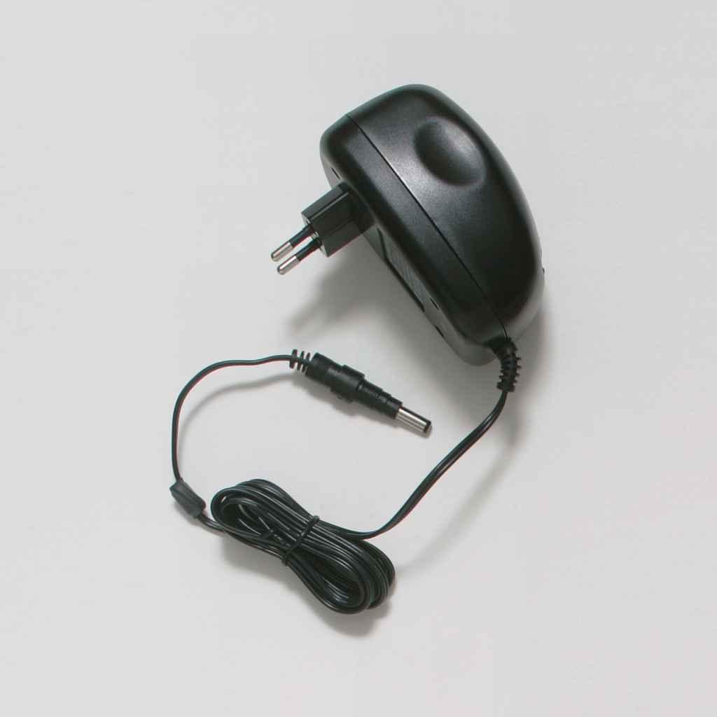 The picture shows a black power supply with a Euro plug, which is used to power electrical devices. It has an outgoing cable with a round plug for connection to various devices or experimental needs.