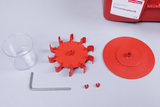 The picture shows various parts of an experiment set for physics lessons, including a transparent beaker, a red gear system, a round platform and some connecting elements. These components are designed for practical physics experiments.