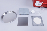 The picture shows various experimental materials, including an aluminum plate, a small glass beaker, a candle and a metal bowl, which can be used for teaching elementary physics. These materials are arranged in a red box from Cornelsen, which is intended for educational purposes.