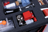 The picture shows a set of different experimental materials arranged in a foam pad. Among other things, you can see a glass flask, a metal bell, an orange button probe and various small tools.