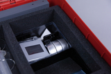 The picture shows a red box padded with black foam and containing various experimental devices. Visible are, among other things, a device with a display and a silver cylinder unit that can be used for educational experiments.