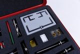 The picture shows an experiment box with various tools and components arranged on a foam interior. In the middle there is a gray circuit board with a circuit pattern and various other parts for experimentation.