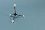 The image shows a model of a molecule with three gray connecting elements and a black central sphere connected to three white spheres. It is intended for illustrating chemical structures in educational settings.