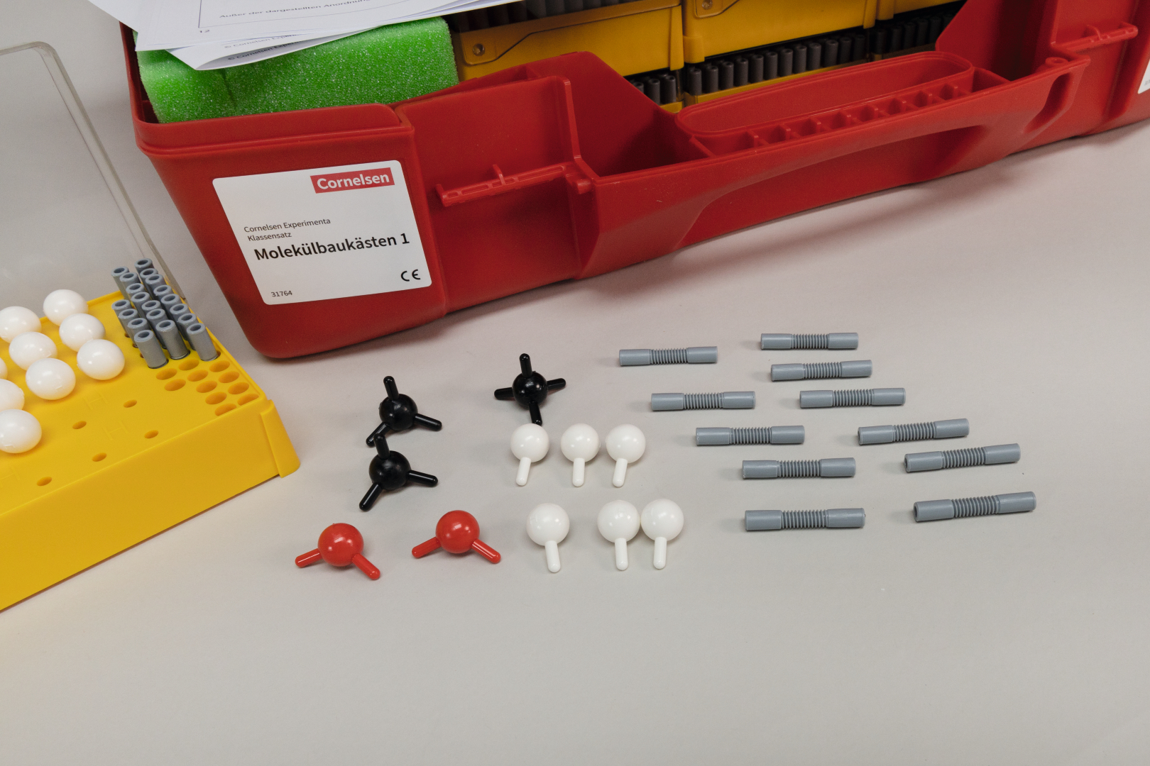 The picture shows a molecule construction kit with various colorful building blocks that are used to construct molecules. Next to the box are some elements, including black, white, red and gray pieces that represent different atoms.