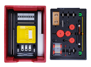 The picture shows an experiment box that is divided into two compartments and contains various physical components. The left side contains a yellow bowl and rods, among other things, while the right side provides rollers, weights and other materials for experiments.