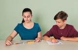 The picture shows two students at a table. The female student is using an experimental device while the male student is taking notes on a worksheet.
