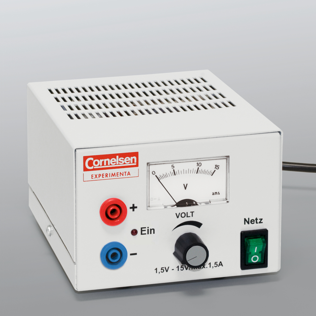 The picture shows an electrical experimental device with a white housing that has connections for positive and negative poles and a rotary control for voltage adjustment. A scale shows the voltage in volts and the device has a power switch.