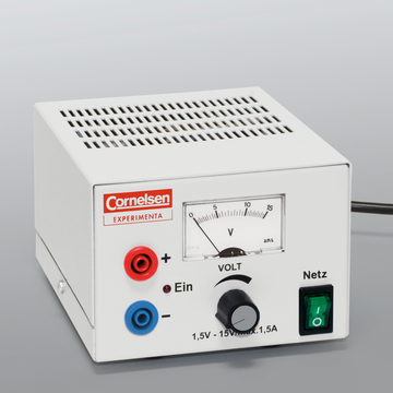 The picture shows an electrical experimental device with a white housing that has connections for positive and negative poles and a rotary control for voltage adjustment. A scale shows the voltage in volts and the device has a power switch.