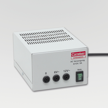 The picture shows a white power supply unit with a ventilation grille and three connections for voltages of 0, 6V and 12V. It is a product of the Cornelsen brand, which is designed for experimental use in education.