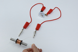 The picture shows an experimental setup with two red cables connected to a power source with a measuring device. In a person&#39;s hand is a transparent tube with a copper wire winding, which is part of the experiment.