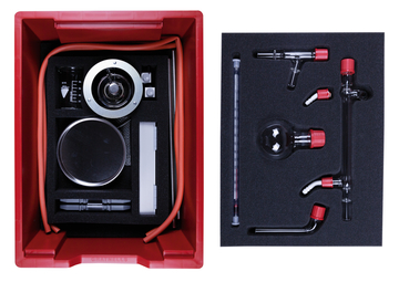 The picture shows an experiment kit packed in a red box. The contents include various glassware, a scale and tubing that can be used for educational chemistry experiments.