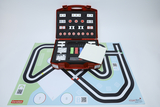 The image shows a red suitcase filled with various experiment materials, as well as a colorful playing field with road patterns and QR codes. The suitcase contains components for hands-on experiments designed to support learning in educational settings.