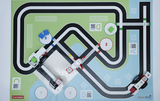 The image shows a colorful play mat with a branching road layout and several stations marked with numbers and QR codes. Model vehicles are placed on the mat, suggesting an interactive learning environment.