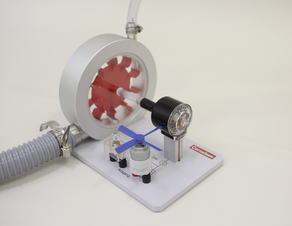 The picture shows an experimental device for demonstrating air pressure and mechanics. It consists of a red wheel, a pressure gauge and a small motor, which together provide an instructive representation of physical principles.