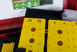 The picture shows yellow experiment plates with various holes and recesses that can be used for scientific experiments. In the background you can see an overview of other experiment materials, while transparent tubes are in a dark box.