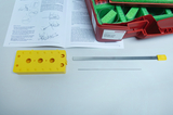 The picture shows a yellow holder with three holes and two tools: a long, flat metal rod with a yellow handle and a thin metal rod. In the background is an open manual with instructions for sound experiments.