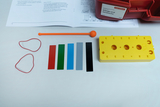 The picture shows materials for experiments on sounds and noises, including a yellow plate with holes, colored stripes and rubber bands. There are also instructions on the table that describe how to carry out experiments.