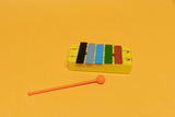 The picture shows a colorful xylophone on a yellow background. Next to the xylophone is an orange mallet that is used to play the instrument.