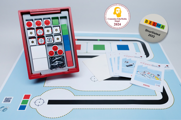 The picture shows a set for experimental needs that contains various components in a red box, including cubes and colored blocks, as well as instructions and a special pad with a track layout. It is suitable for educational and experimental purposes in the German education system.
