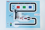 The image shows an interactive learning environment with a miniature vehicle and a set track on a blue background. Several colored fields as well as QR codes are placed on the layout to encourage experimentation.
