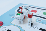 The image shows an assembled robot model made of building blocks, placed on a printed base. The base contains various markings and areas that are probably used for programming or tracing purposes.