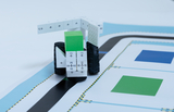 The image shows a vehicle made of building blocks placed on a printed base. The base has different colored areas and lines that are probably used to program or control the vehicle.