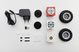 The picture shows an arrangement of various components of an experiment kit, including a charger, USB stick, electronic blocks and wheels. The parts are designed to enable students to program and build robots.
