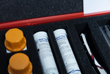 Inside a red case are several test containers for medical tests, including glucose and protein tests. The equipment is carefully arranged and surrounded by foam to protect it during transport.