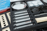 A set for experimental applications in educational settings includes several thermometers, a metal bowl, sample containers, and safety goggles. The assembly is carefully placed on a foam tray to protect and organize the materials.