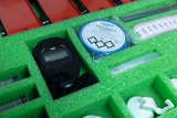 The box contains various experimental materials, including a stopwatch, containers, a roll of Vaseline, and measuring instruments. The green foam padding ensures the equipment stays securely in place during transport.