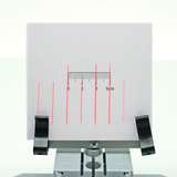 A gray surface depicts vertical red lines printed on a white sheet of paper. A small scale with centimeter markings is located in the center to measure the distances between the lines.