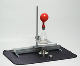 Ein Erlenmeyerkolben mit einem roten Gummiballon steht auf einem Metallgitter an einem Stativ. Darunter befindet sich ein Spiritusbrenner auf einer schwarzen Unterlage.