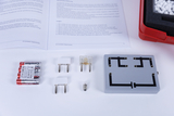 Ein Physik-Experimentierset besteht aus einer grauen Schalttafel, Batterien und verschiedenen Steckelementen. Im Hintergrund liegt eine passende Anleitung von Cornelsen Experimenta auf einem Tisch.