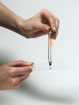 Zwei Hände halten eine leuchtende Gasentladungsröhre über eine transparente Kunststoffplatte. Es handelt sich um ein physikalisches Experiment zur Demonstration von Lichtbrechung oder Polarisation.