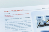Ein Auszug aus einem Lehrbuch erklärt die korrekte Handhabung einer Netzspule. Textpassagen und mathematische Formeln zur Impedanz sowie ein Foto des Bauteils sind zu sehen.